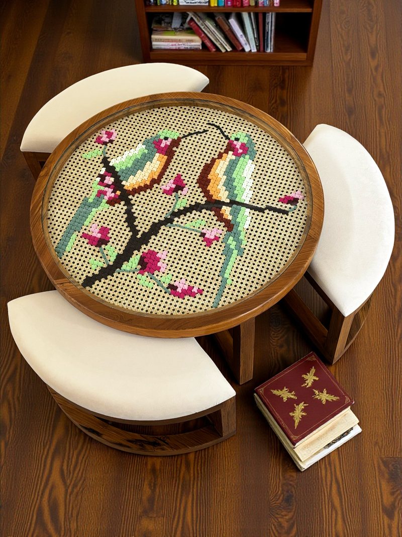 A round coffee table with a thread on cane top of two birds on a flowering branch, with curved cushioned seats tucked around it.